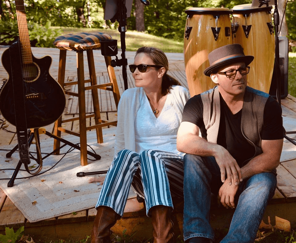 Roxy & Proxy - Acoustic duo with woman and man sitting with guitar and percussion setup